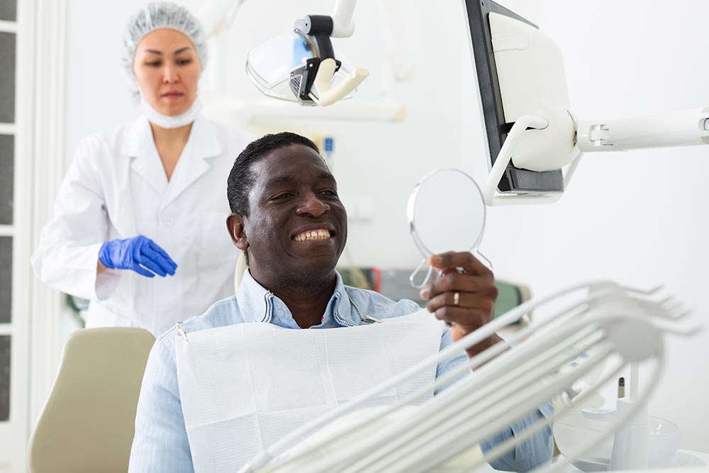 A Man Smiling Holding a Dental Object with a Dentist at his Back