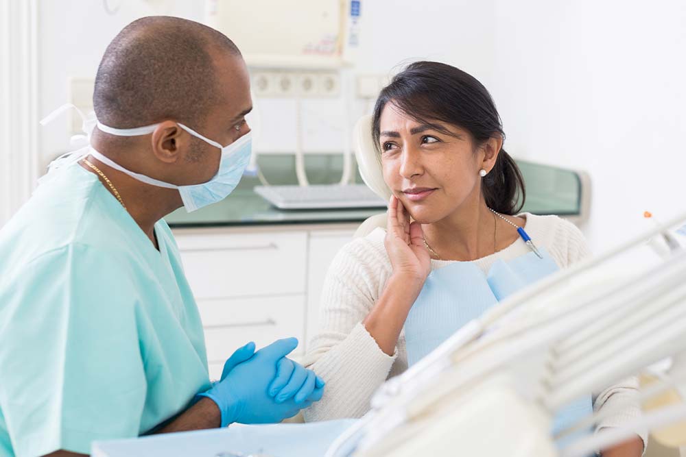 The Dentist Touches the Face of his Patient if she feels Tooth Pain